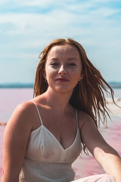 Linda mujer adolescente con vestido blanco sentada en un increíble lago rosa