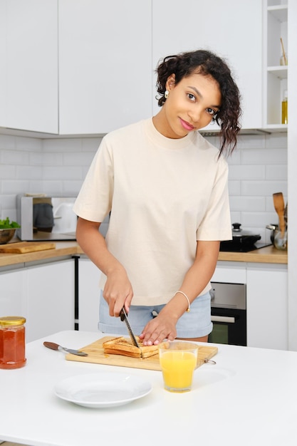 Linda mujer africana cortando tostadas dulces con mermelada a la mitad