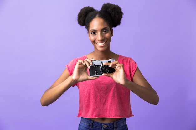 Linda mujer afroamericana sonriendo y sosteniendo una cámara retro, aislado
