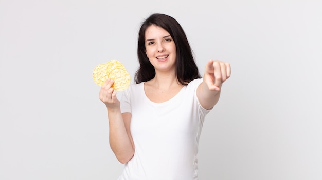 Foto linda mujer apuntando a la cámara eligiéndote y sosteniendo una dieta de pasteles de arroz