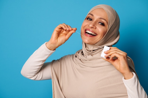 Linda mujer árabe con la cabeza cubierta y una sonrisa perfecta con un hilo dental y posando