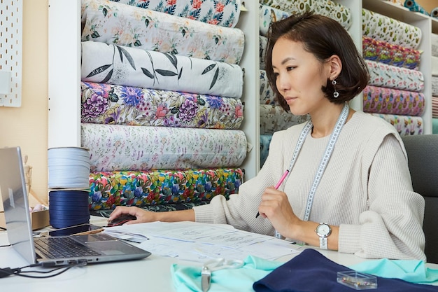 Foto linda mujer asiática diseñadora de moda trabajando en una laptop en el taller