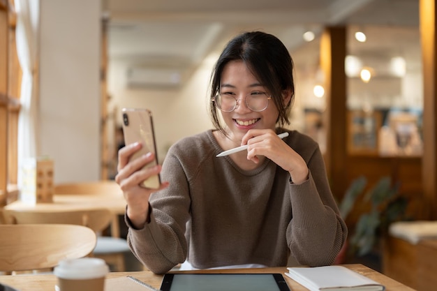 Una linda mujer asiática usando su teléfono inteligente mientras estaba sentada en una mesa en una cafetería