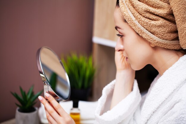 Linda mujer en el baño haciendo procedimiento cosmético para el cuidado de la piel facial