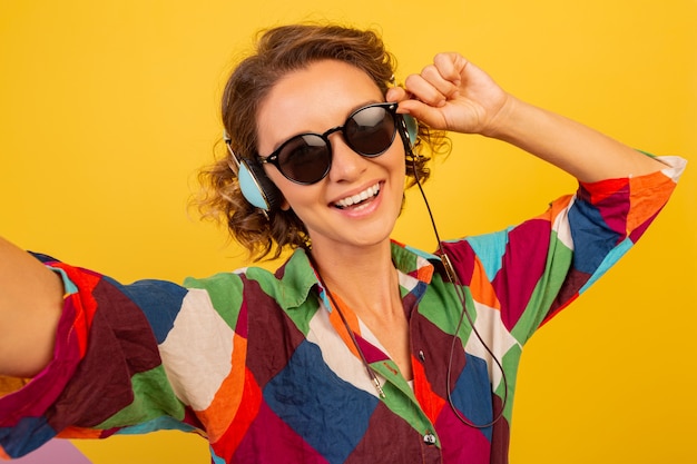 Linda mujer bonita con auriculares envía un beso a la cámara y hace un autorretrato sobre una pared amarilla