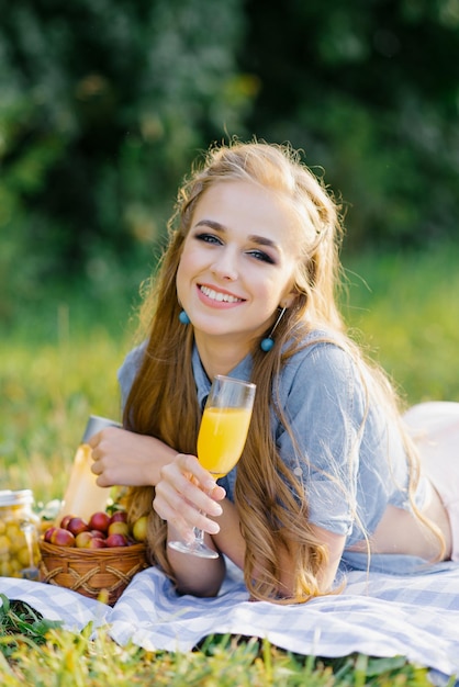 Linda mujer bonita con un vaso de jugo en la mano está acostada sobre una manta en un picnic de verano
