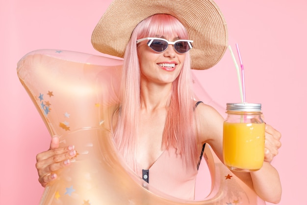 Linda mujer con cabello rosado en traje de baño y gafas de sol con cóctel tropical y estrella inflable para