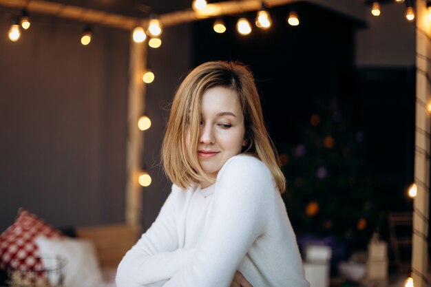 Linda mujer con cabello rubio posa en una acogedora habitación decorada para Navidad