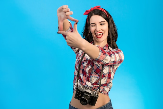 La linda mujer con una cámara retro gesticulando sobre el fondo azul.