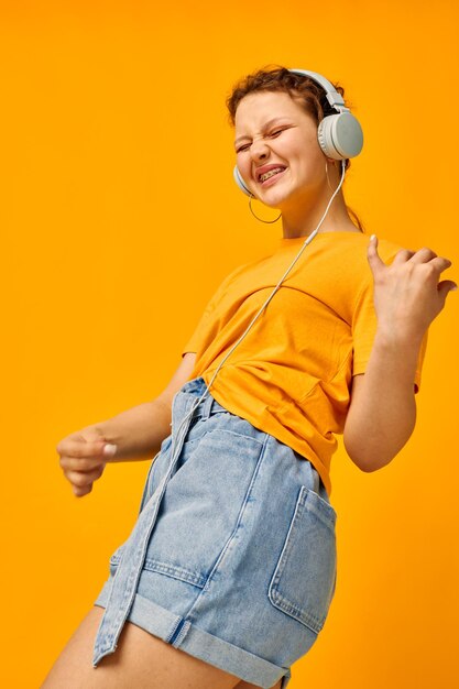 Linda mujer camiseta amarilla auriculares entretenimiento música diversión fondo amarillo inalterado