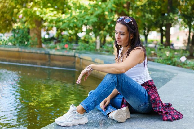 Linda mujer caucásica se sienta junto a una fuente en el parque en un día soleado disfruta de la frescura