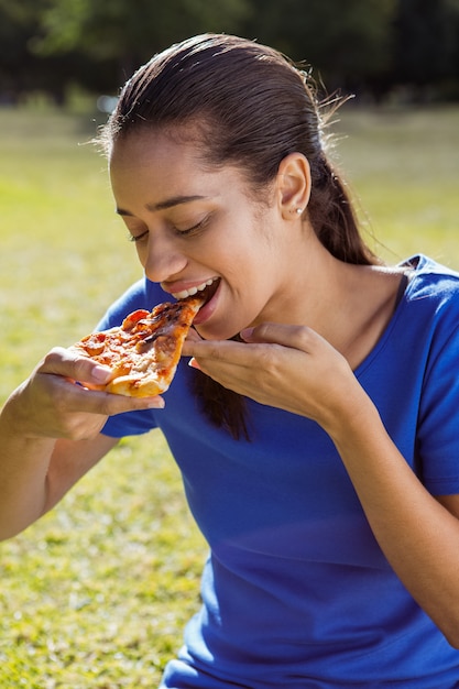 Linda mujer comiendo pizza en el parque