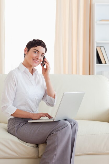 Linda mujer con una computadora portátil y un teléfono mirando a la cámara