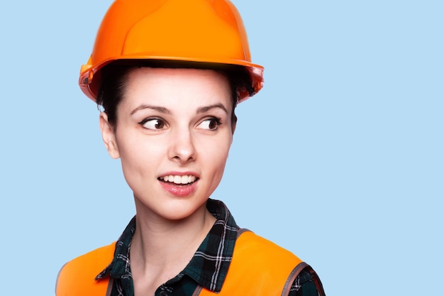 linda mujer en construcción casco y chaleco naranja fondo azul
