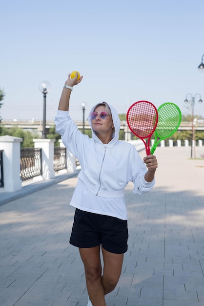 Una linda mujer deportiva sostiene raqueta y pelota al aire libre