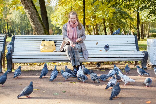 Linda mujer descansando en el parque y alimentando palomas