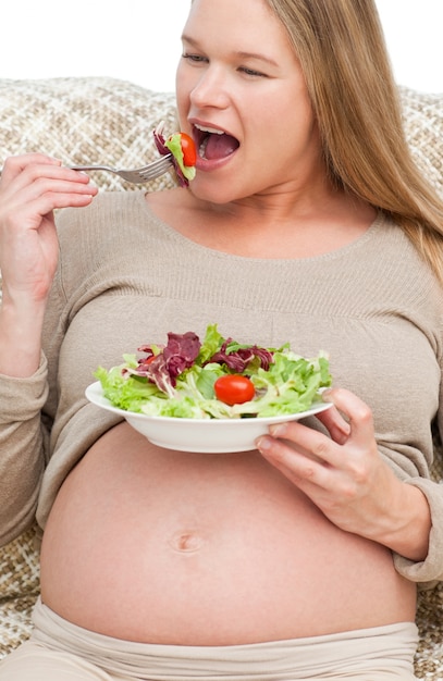 Linda mujer embarazada comiendo una ensalada sentado en el sofá
