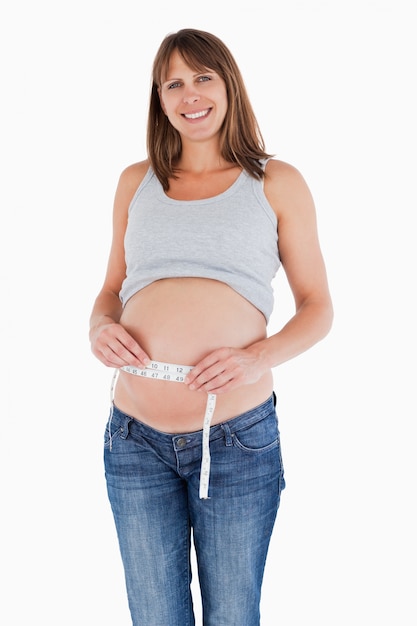 Linda mujer embarazada midiendo su vientre mientras está de pie