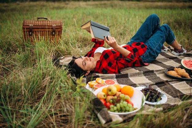Linda mujer se encuentra en cuadros y lee el libro, picnic en la pradera. Viaje romántico, felices fiestas