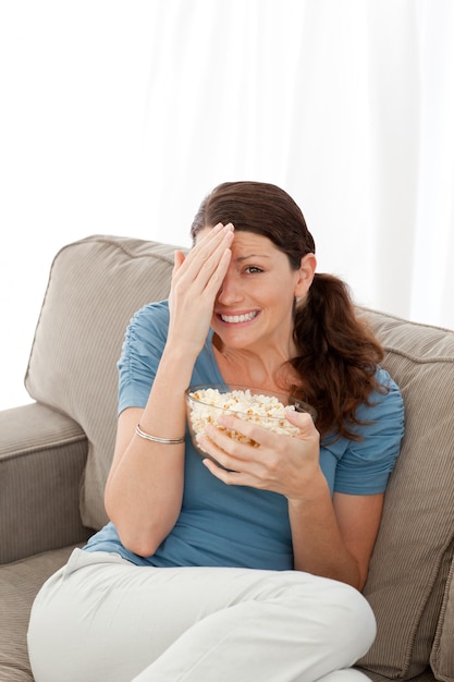 Linda mujer escondiendo su rostro mientras ve una película de terror