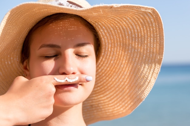 Linda mujer está posando con bigote dibujado con crema solar en su dedo debajo de la nariz en el fondo del mar.