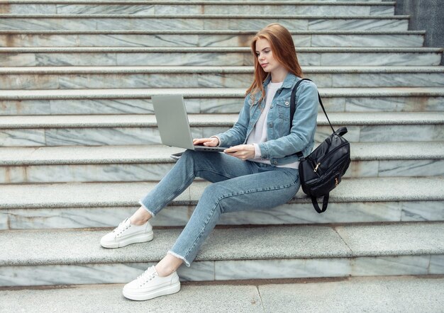 Linda mujer estudiante con laptop sentada en las escaleras al aire libre Educación a distancia