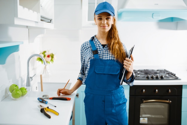 Linda mujer fabricante de muebles en uniforme sostiene el cuaderno en la cocina.