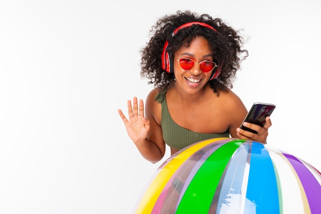 Linda mujer con grandes auriculares rojos, gafas de sol y soportes de teléfono con pelota de goma grande aislado en blanco