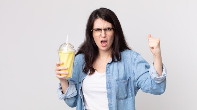 Linda mujer gritando agresivamente con una expresión enojada y sosteniendo un batido de vainilla