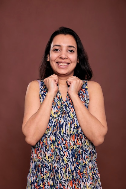 Linda mujer india sonriente sosteniendo puños apretados en el retrato de las mejillas. Señora alegre tocando la cara con las manos, modelo de pie con expresión despreocupada, mirando a la cámara, vista frontal