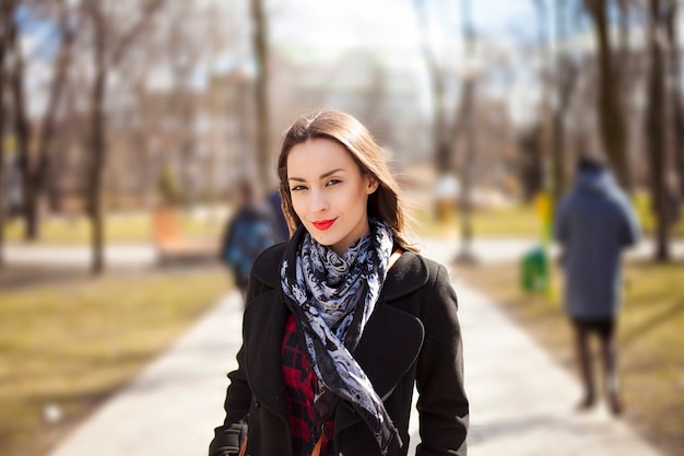 Linda mujer joven confiada en abrigo está caminando por el parque de la ciudad de otoño