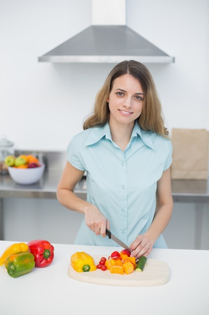 Linda mujer joven cortar verduras en la cocina