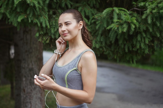 Linda mujer joven escuchando música mientras trota por el camino en un parque verde