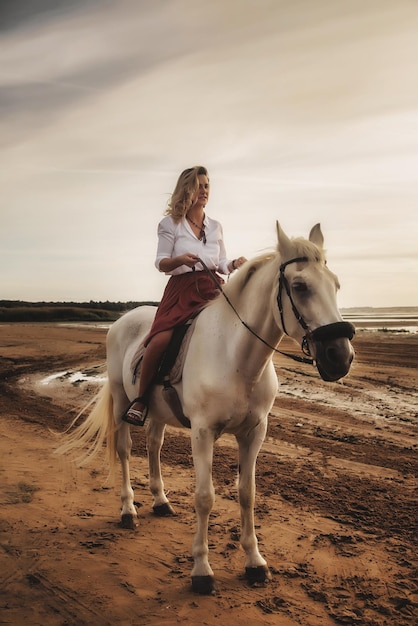 Linda mujer joven feliz a caballo en la playa de verano por mar