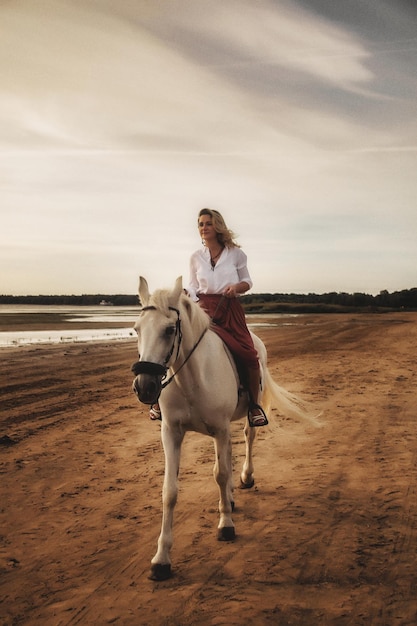 Linda mujer joven feliz a caballo en la playa de verano por mar