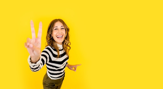 Linda mujer joven feliz con camisa a rayas blanco y negro hace el signo de la victoria