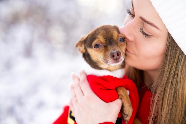 Linda mujer joven en invierno besa a su perro. Chica en la nieve con una mascota chihuahua