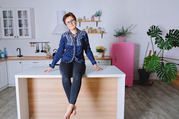 Linda mujer joven en jeans azul sentado en su brillante cocina limpia