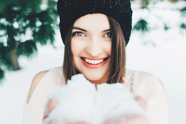 Linda mujer joven jugando con nieve en el exterior. Retrato de una niña feliz. Mira a la cámara.