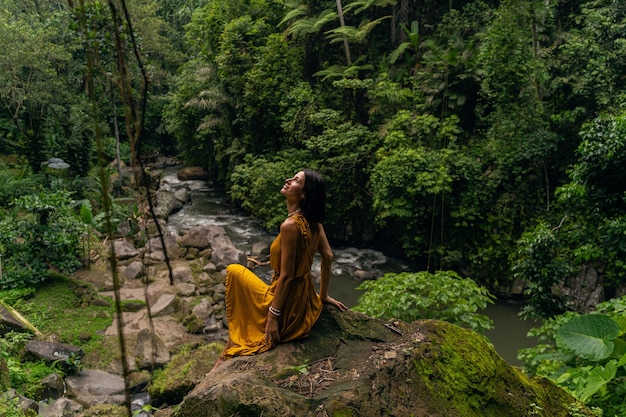 Foto linda mujer joven manteniendo una sonrisa en su rostro mientras mira hacia arriba a las plantas exóticas en la jungla