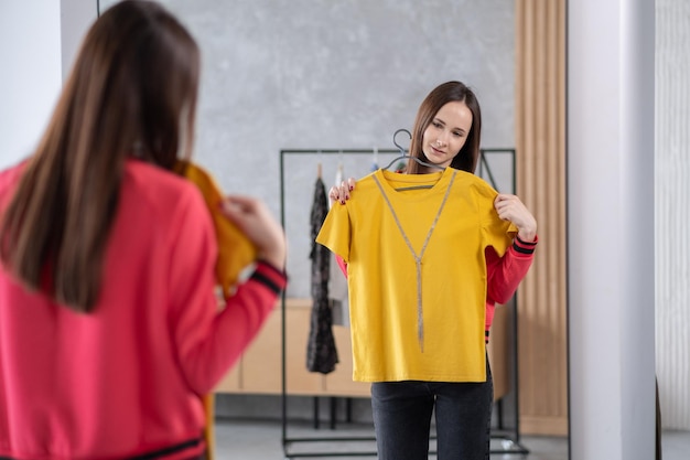 Linda mujer joven de pie frente al perchero y tratando de elegir ropa para el trabajo o caminar Selección de un estilista de vestuario de compras