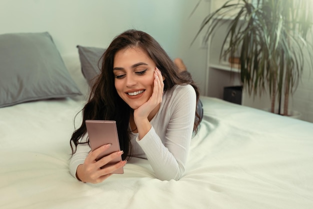 Linda mujer joven en pijama usando el teléfono en la cama