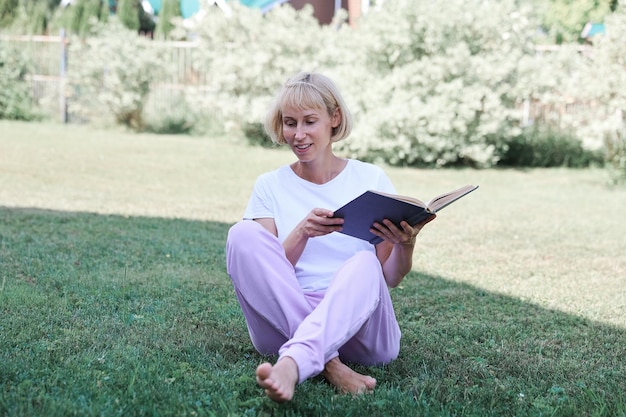 Linda mujer joven sentada en la hierba y leyendo el libro