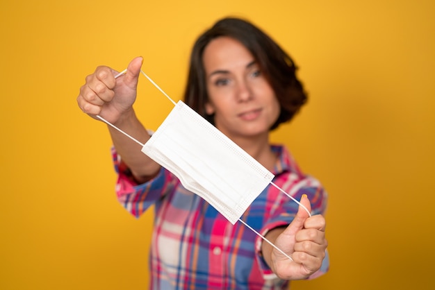 Foto linda mujer joven tiene máscara protectora en primer plano. aislado sobre fondo amarillo. concepto de cuarentena. copie el espacio.