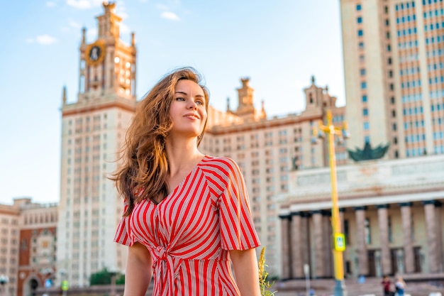 Linda mujer joven con un vestido rojo posa con el telón de fondo de la principal Universidad de Moscú