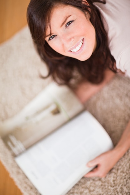 Linda mujer leyendo una revista mientras se está acostado sobre una alfombra