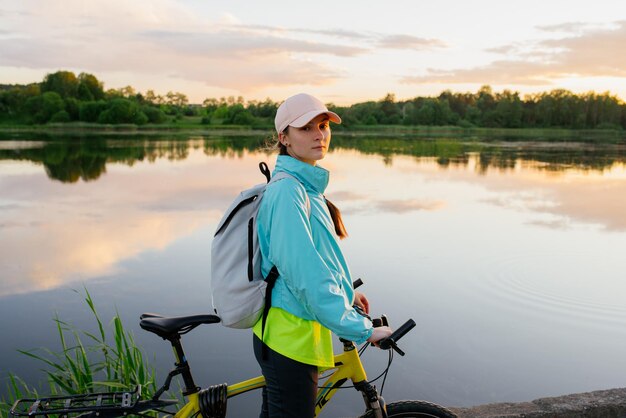 Linda mujer montando en bicicleta de montaña durante la puesta de sol en la costa sobre el lago Vacaciones de viaje de verano