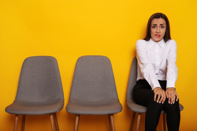 Linda mujer morena moderna elegante está sentada en la línea de sillas en cita de entrevista de trabajo