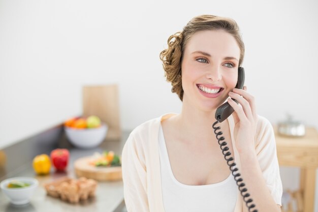 Linda mujer pacífica llamando con un teléfono en su cocina