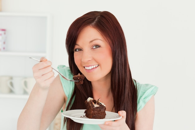 Linda mujer pelirroja comiendo pastel en la cocina